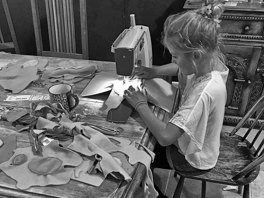 Young girl sitting at a desk using a sewing machine.