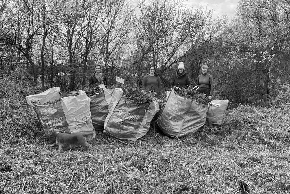 Four people standing behind large bags of cleared material.