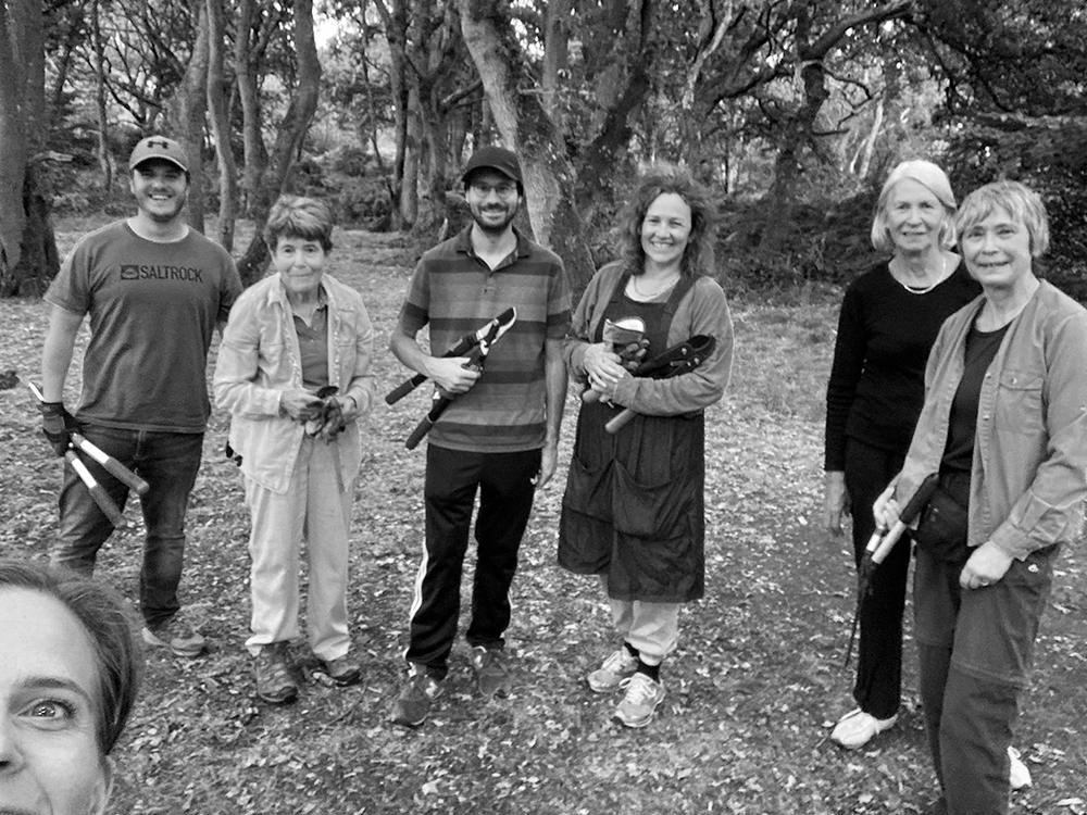 Six people holding tools. The photographer's face is partly visible close up in the corner.