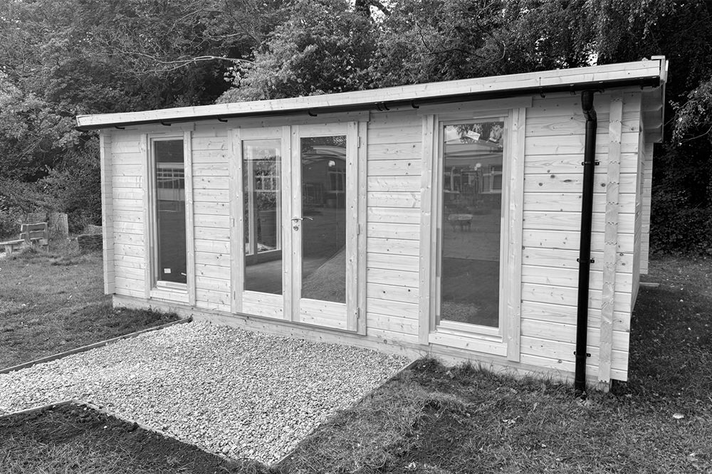 Wood-clad cabin with a tall window either side of the French doors in the middle.