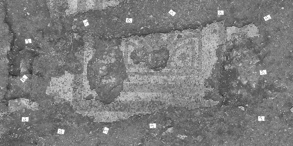 Aerial view of a partially unearthed mosaic floor showing its reddish brown pattern.